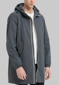 Veste légère grise avec capuche, poignets élastiques, fermeture éclair sur le devant et détails de fermeture éclair contrastants. Présente une coupe décontractée et une texture douce.