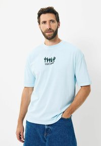 Tricou din bumbac de culoare bleu deschis, cu mânecă scurtă și gât rotund. Prezentând un grafic cu un cactus verde pe față. Purtat împreună cu şorturi din denim.