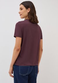 Haut à manches courtes en coton bordeaux, coupe décontractée, col rond, texture lisse, avec un jean en denim visible à la taille.