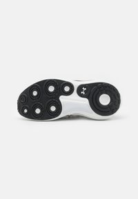 Semelle de chaussure avec motifs de bande de roulement circulaires noirs, semelle intermédiaire blanche et logo Under Armour près de la voûte sur un fond clair uni.