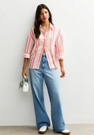 Lichtgewicht, roze en witte gestreepte shirt, met knoopsluiting; gecombineerd met hoge, vervaagde blauwe wijde jeans en witte sneakers. Kleine metalen tas.
