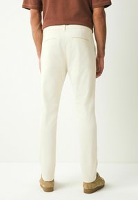 Pantalones blancos con corte recto, con bolsillos traseros y cierre oculto. Combinados con zapatos de ante marrón. Textura de tela casual.