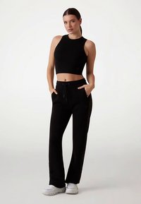 Schwarzes Crop-Top und lockere schwarze Hosen aus weichem Material, mit Kordelzug, seitlichen Taschen und weißen Sportschuhen.
