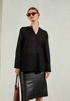 Blusa preta transparente com decote em V, mangas longas e punhos abotoados, combinada com uma saia lápis de couro preta, segurando uma bolsa bordô.