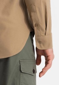 Lichtbruine shirt met knoopmanchetten, gecombineerd met olijfgroene cargoshorts met een flapzak en een donkere knop. Gestructureerde stof.