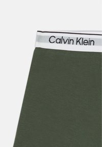Olivenfargede Calvin Klein undertøy med hvit midjebånd som har svart logo og grå stripe på midjebåndet.