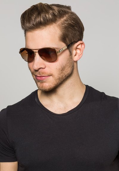 Sunglasses with brown gradient lenses, thin gold frames featuring striped accents, worn with a black t-shirt.