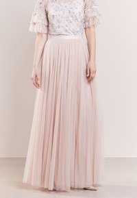 Jupe en tulle rose clair avec un design plissé et fluide. Elle présente une taille ajustée et semble superposée pour plus de volume et de texture.