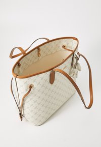 Un sac fourre-tout de couleur crème avec un extérieur à motifs et des poignées en cuir marron, vu de dessus montrant son intérieur spacieux.