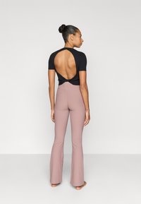 Μαύρο κοντομάνικο τοπ με ανοιχτή πλάτη και λεπτομέρεια στριφογυρίσματος, συνδυασμένο με ανοιχτό ροζ καμπανέ παντελόνια από λείο ύφασμα.