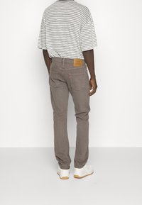 Šedé džíny s rovnými nohavicemi, které mají koženou záplatu na zadním pasu a kontrastní červený štítek na zadní kapse. Kombinují se s proužkovaným tričkem.