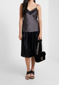 Camisola in satin grigio scuro con pizzo, gonna pieghettata nera, sandali neri con tacco e borsa in velluto nera con hardware dorato.