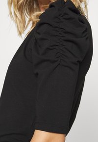 T-shirt nero con maniche puff arricciate, in tessuto morbido e silhouette aderente, che presenta una texture liscia e dettagli di cuciture pulite.