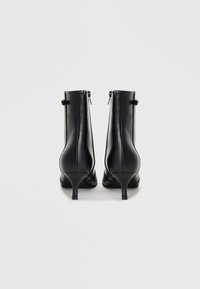 Bottines en cuir noir avec un bout pointu, un talon sculpté et une fermeture éclair sur le côté, ornées d'un petit accent doré près de la cheville.