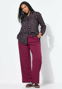 Zwarte button-up shirt met een roze bloemenpatroon, gecombineerd met losse bordeauxrode broek en een paar bruine sneakers, tegen een eenvoudige witte achtergrond.