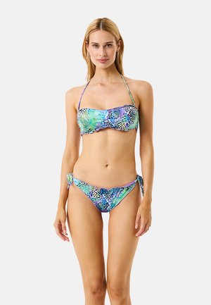 Donna con bikini bandeau multicolore a stampa animalier con spalline a collo halter, in piedi su uno sfondo semplice e chiaro.