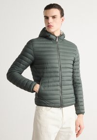 Polstret grøn jakke med hætte, med en frontlynlås, ribbet struktur og sidelommer. Glat stof med en tætsiddende design.