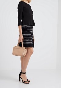 Schwarzes Peplum-Top kombiniert mit einem schwarz-weißen gestreiften Bleistiftrock. Hält eine beige Handtasche. Schwarze, geschnürte Sandalen mit hohen Absätzen.