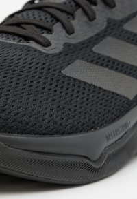 Black athletic shoe featuring a breathable mesh upper, smooth synthetic accents, textured sole, and three metallic stripes on the side.
