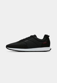 Black low-top sneaker with white sole, lace-up design, subtle "HUGO" branding, and small red stitching detail near heel.