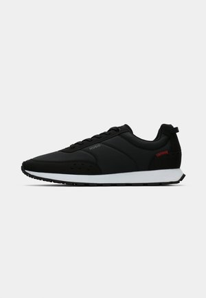 Black low-top sneaker with white sole, lace-up design, subtle "HUGO" branding, and small red stitching detail near heel.