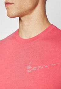 Růžové bavlněné tričko s jemným bílým logem Nike swoosh na levé hrudi, kulatým výstřihem a hladkým, lehkým materiálem.