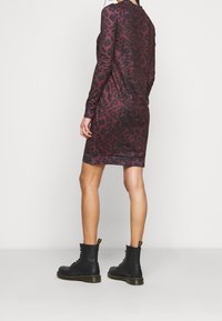 Långärmad klänning i vinröd med svart leopardmönster, gjord av elastiskt tyg. Matchad med svarta snörboots med gula detaljer.