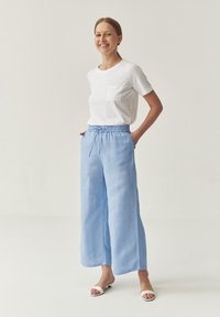 Lichtblauwe linnenbroek met wijde pijpen en een elastische tailleband, gecombineerd met een witte katoenen t-shirt met een zak aan de voorkant.