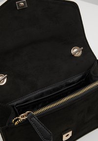 Borsa a tracolla in suede nero con chiusura a scatto magnetico, hardware dorato e una tasca interna con zip foderata in tessuto nero.