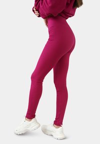 Fitted leggings in een levendige fuchsia kleur, gemaakt van geribde stof met een hoge tailleband, gecombineerd met witte sportschoenen.