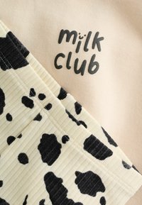 Tela rosa clara con el texto "milk club", combinada con tela crema acanalada con estampado de vaca negro. Diseño texturizado y contrastante.