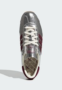 Hõbedane pragunenud nahk sneaker marooni aktsentidega, kreemilised nöörid ja mustriline sisetald, millel on Adidas'i logo. Ümar nina disain.