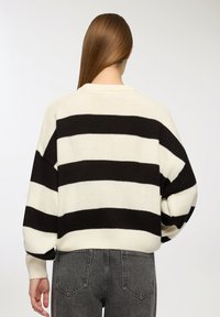 Czarno-biały sweter na drutach w paski o luźnym kroju, z prążkowanymi mankietami i okrągłym dekoltem. Tekstura wydaje się miękka i gruba.