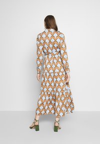 Robe longue présentant un motif floral aux tons bleus et orange. Le tissu est léger avec une taille cintrée et une jupe évasée.