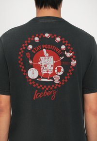 Czarna bawełniana koszulka z grafiką SpongeBoba Kanciastoportego, czerwoną czcionką oraz ikonami jedzenia w okrągłym wzorze w kratkę.