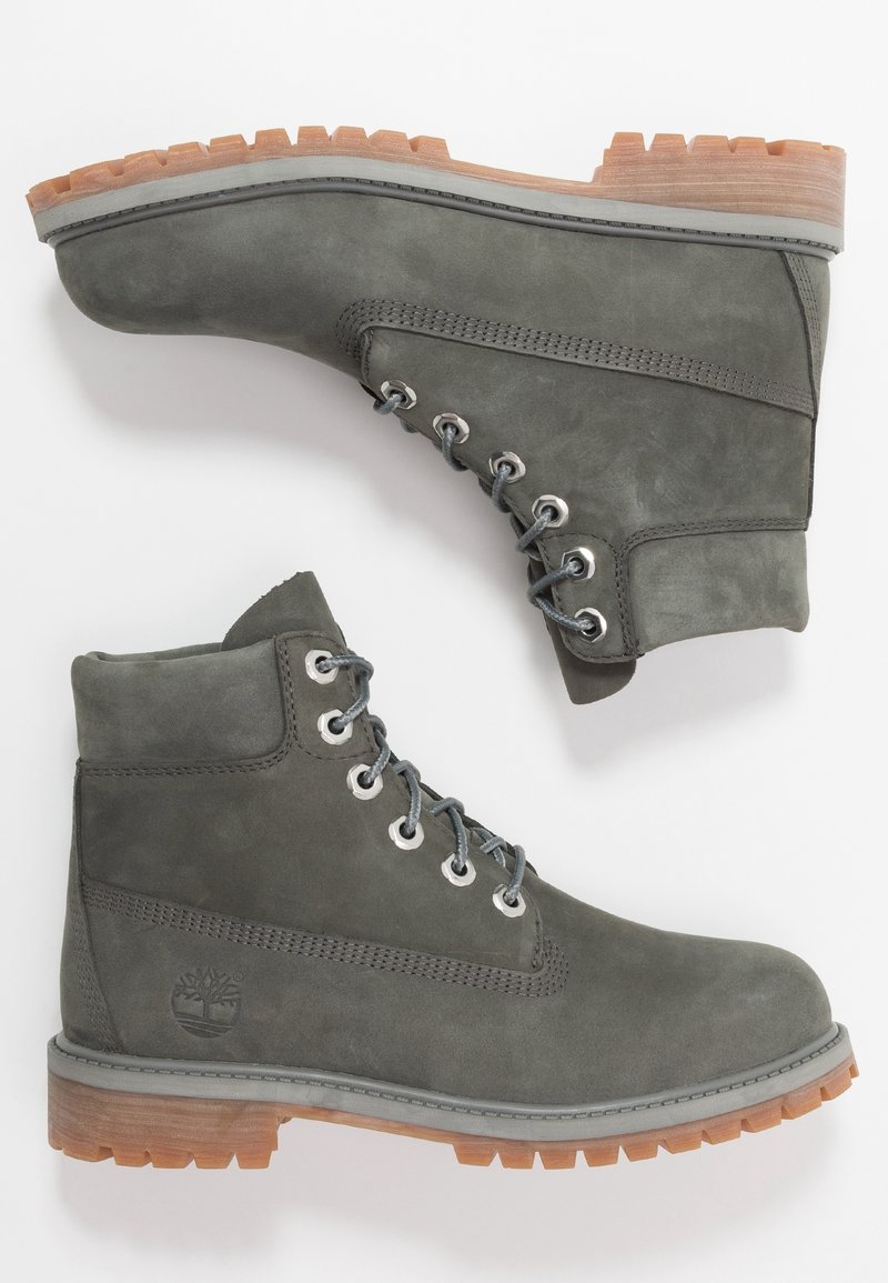 Šedé semišové kotníkové boty mají polstrovaný límec, kovové očka a hnědou gumovou podrážku s hrubým vzorkem pro lepší přilnavost. Vbočené logo.