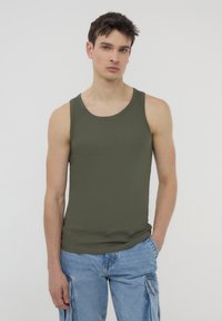 Top senza maniche di colore verde oliva con una texture a coste, scollo rotondo e design aderente, abbinato a pantaloni cargo blu chiaro.