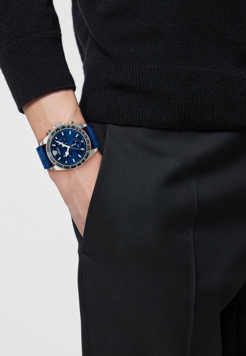 Blaue Chronograph-Uhr mit silbernem Gehäuse, strukturiertem blauen Gummiarmband und blauem Zifferblatt mit kräftigen weißen Markierungen und Zähler. 