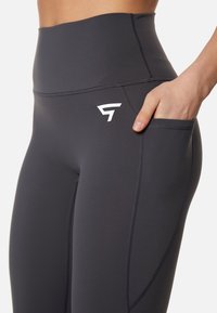 Hoge taille sportleggings in donkergrijs, gemaakt van een gladde, rekbare stof. Bevat een zijzak en contrasterende witte logodetails.