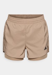 Pantalones cortos deportivos beige con cintura elástica, con aberturas laterales y un logo negro de Adidas en la parte inferior izquierda. Textura suave y tela transpirable.
