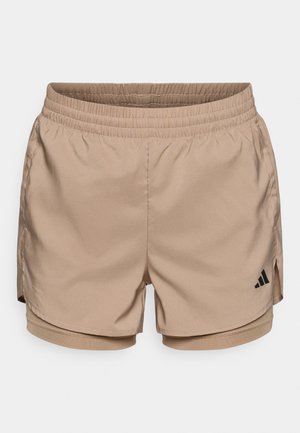 Pantalones cortos deportivos beige con cintura elástica, con aberturas laterales y un logo negro de Adidas en la parte inferior izquierda. Textura suave y tela transpirable.