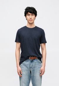 Īsām piedurknēm t-krekls tumši zils, izgatavots no mīksta auduma, saskaņots ar gaiši ziliem džinsa džinsiem un brūnu jostu, ar pieguļošu dizainu.