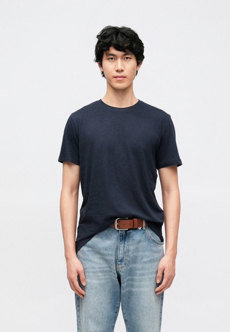 Īsām piedurknēm t-krekls tumši zils, izgatavots no mīksta auduma, saskaņots ar gaiši ziliem džinsa džinsiem un brūnu jostu, ar pieguļošu dizainu.