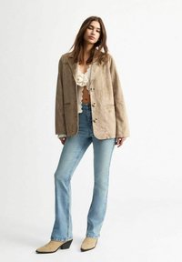 Blazer de ante beige con un corte relajado, gran cuello y cierre de botón, combinado con unos vaqueros de campana azul claro y zapatos de tacón beige.