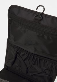Schwarze Kulturtasche mit einem Haken zum Aufhängen, ausgestattet mit mehreren Reißverschluss- und Elastikfächern, aus strapazierfähigem Stoff mit glatter Textur.