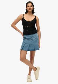 Top sin mangas de punto negro con un diseño de malla estampada, combinado con una falda de mezclilla plisada de un azul claro y zapatillas color crema.