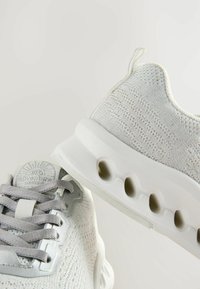 Baskets de sport grises clairs avec un dessus en tricot texturé, un design à lacets et une semelle rembourrée avec des découpes pour la ventilation.