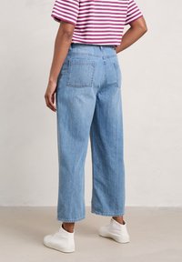 Light blue denim wide-leg jeans with a high waist, featuring two back pockets and a raw hem. Worn with white high-top sneakers.