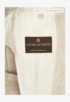 Tessuto beige con un'etichetta marrone textured che recita "OSCAR JACOBSON" e "MADE IN SWEDEN DAL 1903", con dettagli di un bottone e di cuciture.