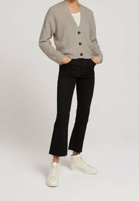 Cardigan gris acanalado con escote en V, botones negros y hombros caídos, combinado con vaqueros negros acampanados y zapatillas blancas altas.